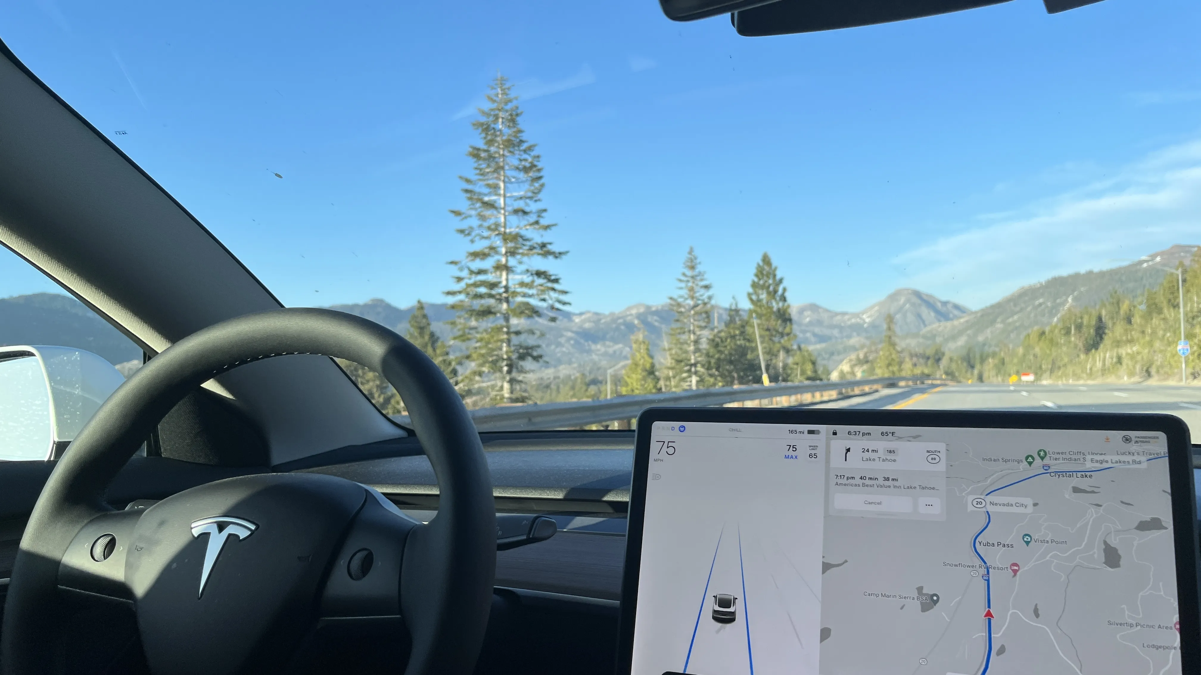 Interior view of a Tesla driving on a mountain highway with navigation touchscreen displayed