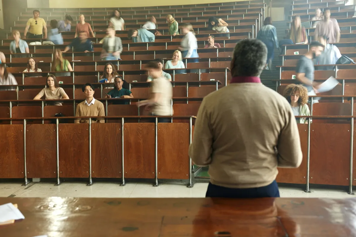 Professor standing at a podium facing students seated in a tiered university lecture hall