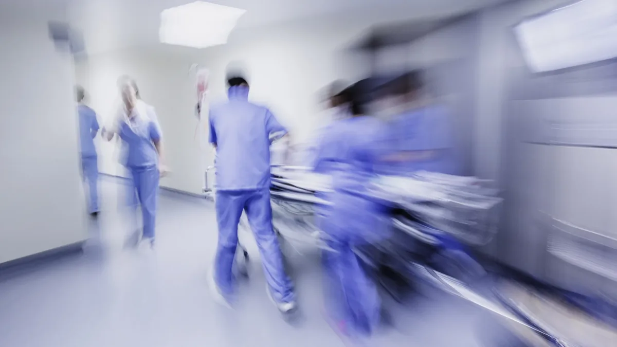 Motion-blurred hospital staff in blue scrubs rushing a patient on a gurney through a hospital corridor