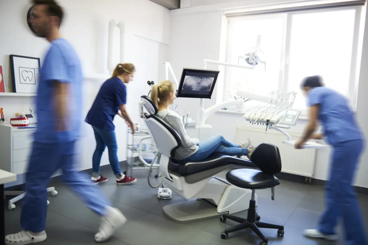 Dental clinic with a patient in the chair and motion-blurred staff in scrubs moving around the treatment room