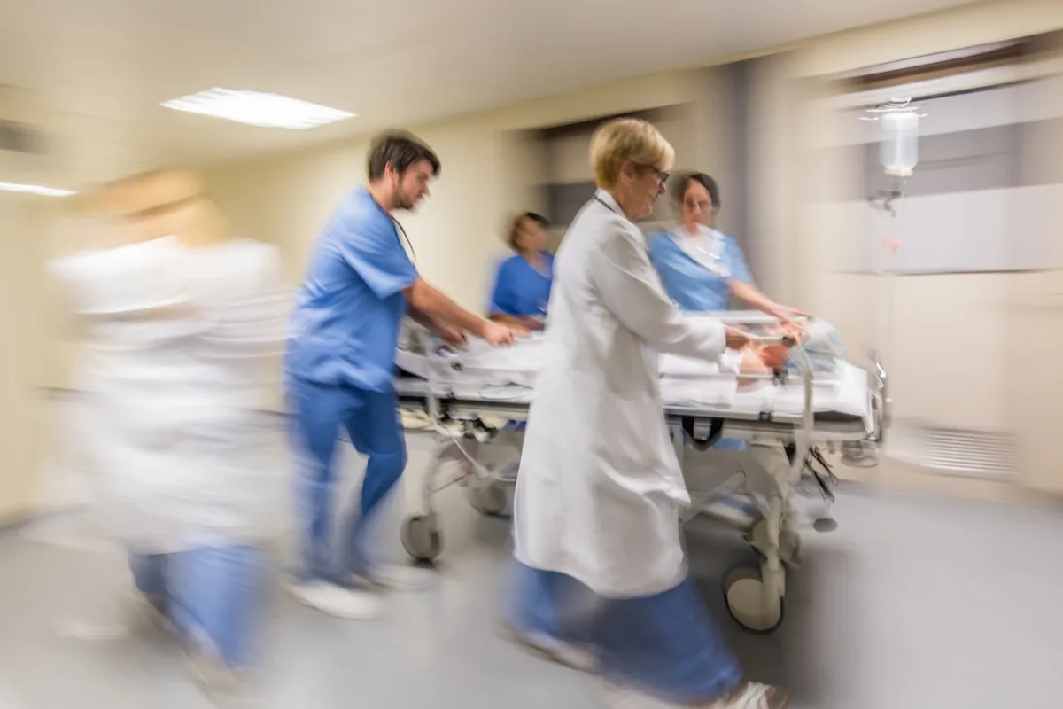 Medical team in scrubs urgently wheeling a patient on a hospital bed through a corridor