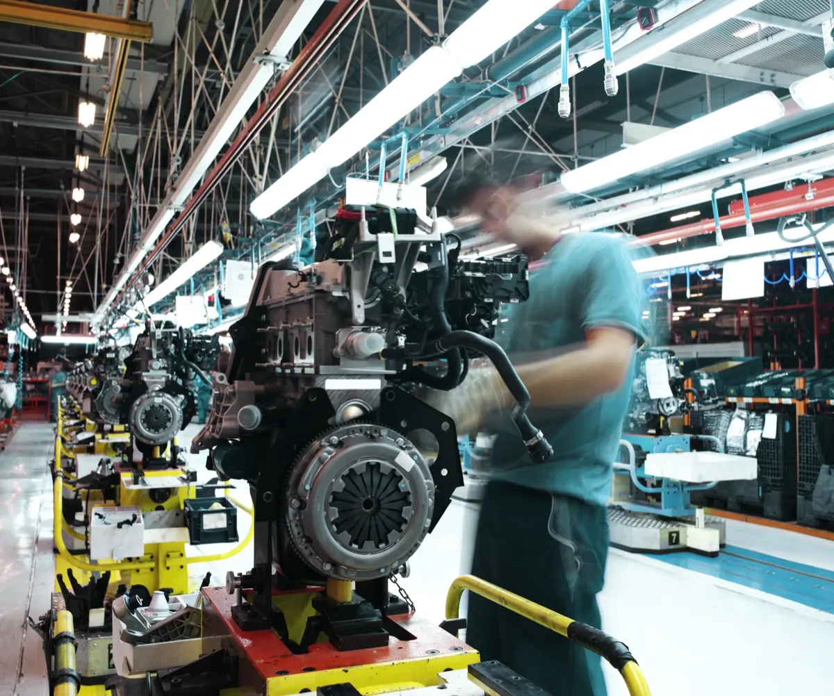 Worker assembling an engine on a factory production line surrounded by industrial machinery and equipment