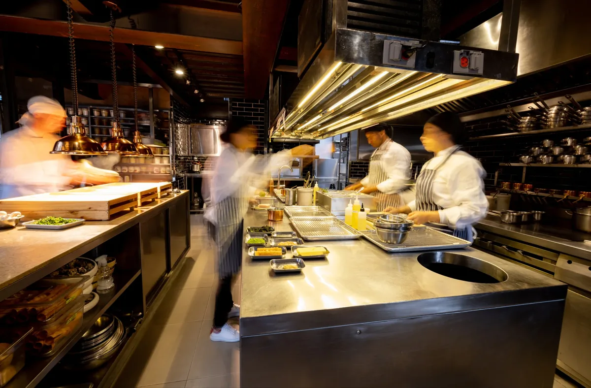Motion-blurred chefs working at speed in a busy commercial kitchen with stainless steel prep stations